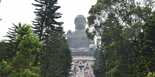 A large statue of the Buddha, with people in the distance walking up a long flight of stairs towards it.
